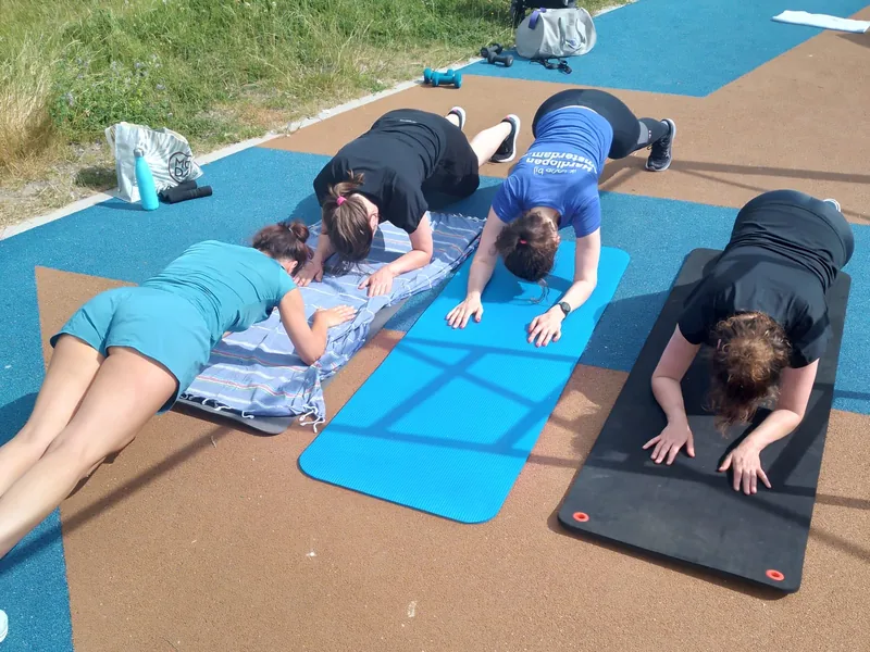 Vier vrouwen doen samen een oefening op matten tijdens het bootcamp buiten