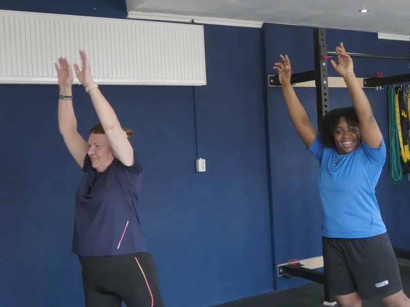 Twee vrouwen strekken hun armen omhoog tijdens de pilatesles bij Convert2Fit