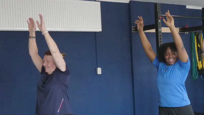 Twee vrouwen strekken hun armen omhoog tijdens een training in de zaal van Convert2Fit